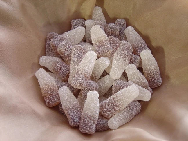 Close-up of a pile of sugared chewy candy shaped as bottles on a beige fabric background. Soft and bendable candy.