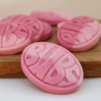 Pink oval marshmallow candies with 'BUBS' text . Bubs are on a wooden board