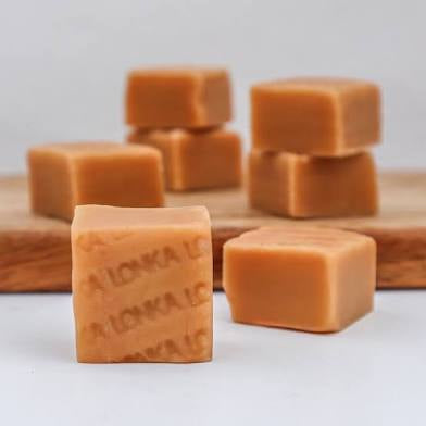 Cubes of caramel-like candies substance on a wooden board with a white background. Marked Lonka