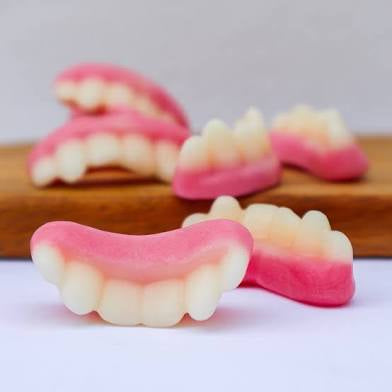 Gumdrop-shaped false teeth gummy candy on a wooden board with a white background. 