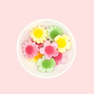 Colorful flower-shaped candies in a white bowl on a pink background