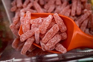 Red scoop filled with with red gummy candies. The candies are cute white coat of sour sugar shaped as old fashion soda bottles. 
