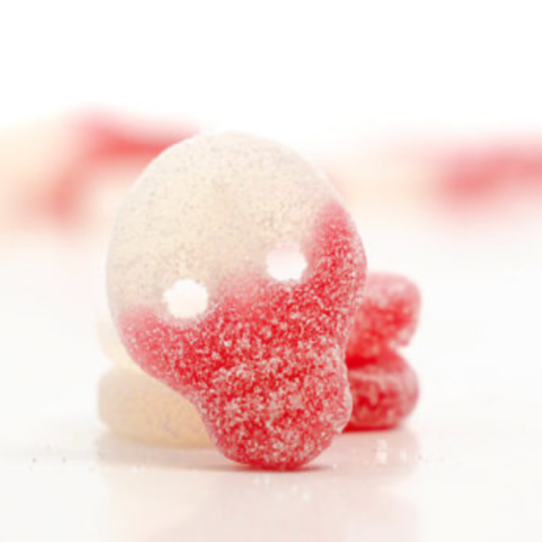 Close-up of red and white gummy candies shaped as a skull covered in sugar on a white background