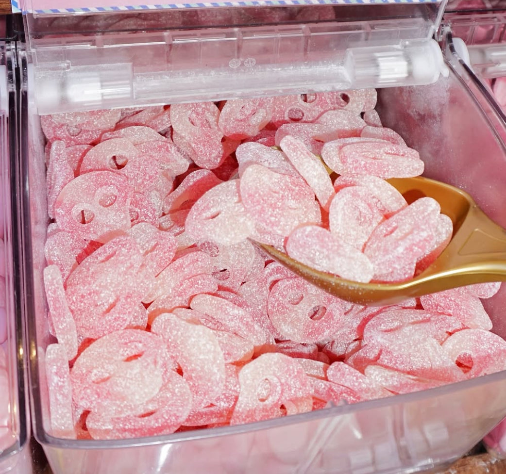 Pink and white gummy candy  n a clear container with a gold scoop.